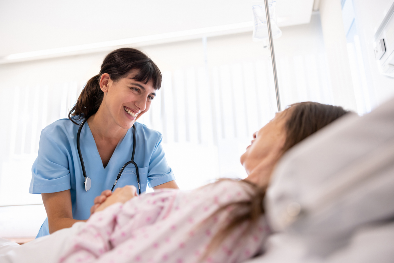 A nurse comforts a patient lying in a hospital bed.