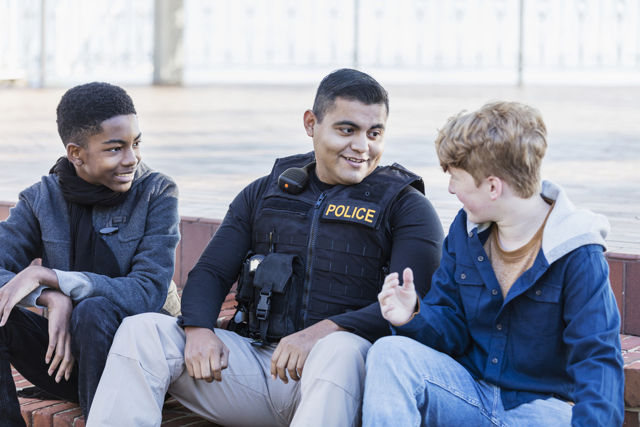 A police officer sits and talks with a two children in a park.