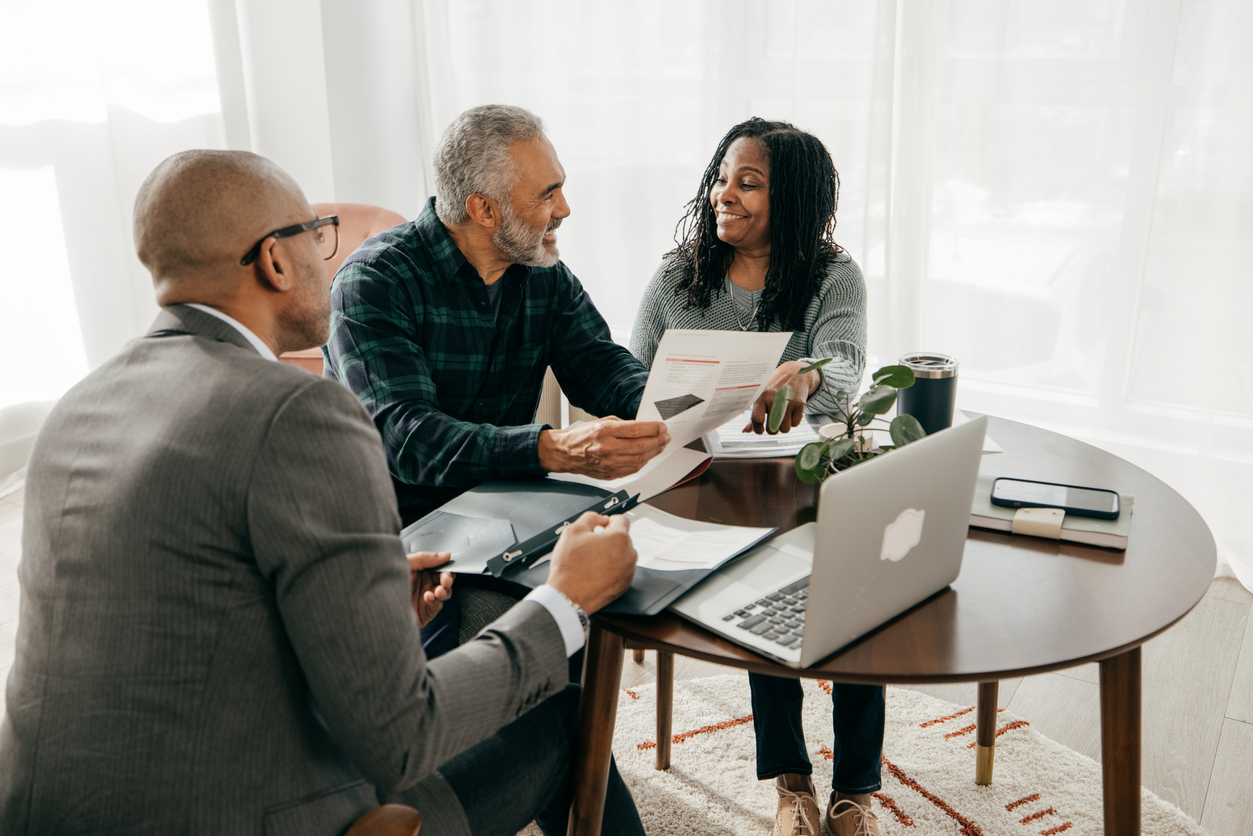 An accountant meets with clients around a table with a laptop and financial documents.