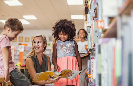 A Kindergarten Teacher Reads a Book to Students in a Library.
