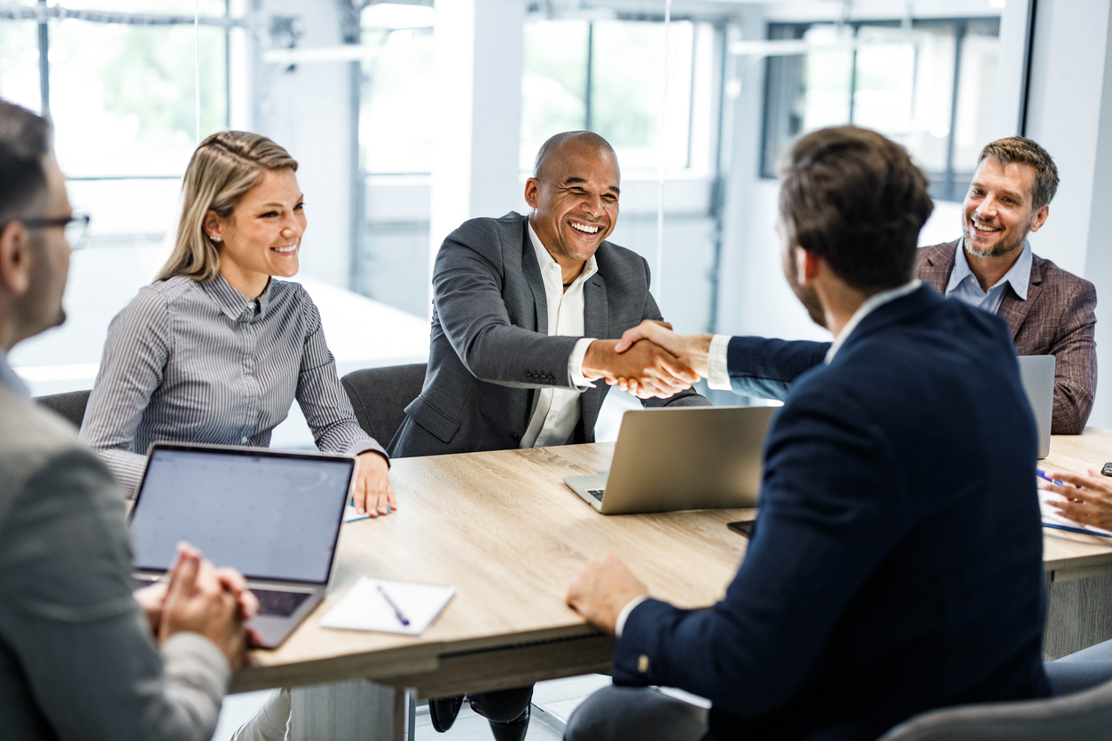 Two Smiling Businesspeople Shake Hands During a Meeting Around a Conference Table.