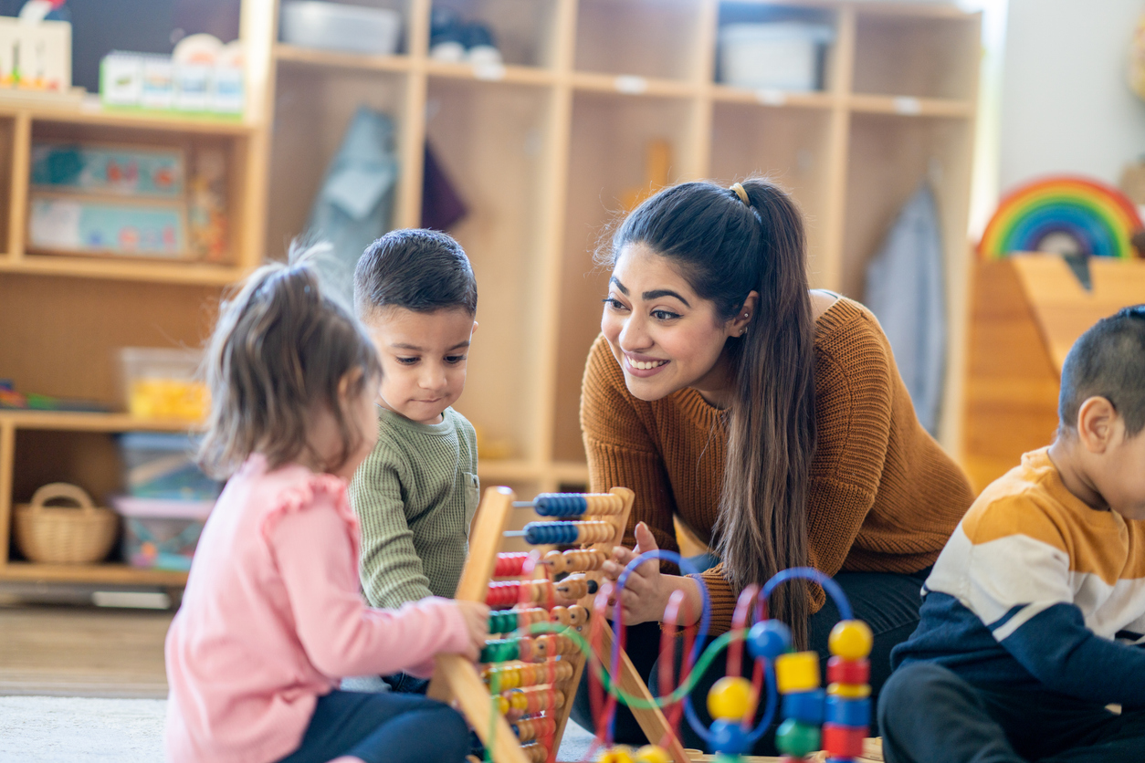 A preschool teacher helps students use a counting toy in a classroom.