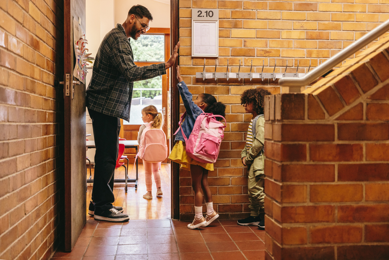 A kindergarten teacher gives a student a high-five outside of a classroom. 