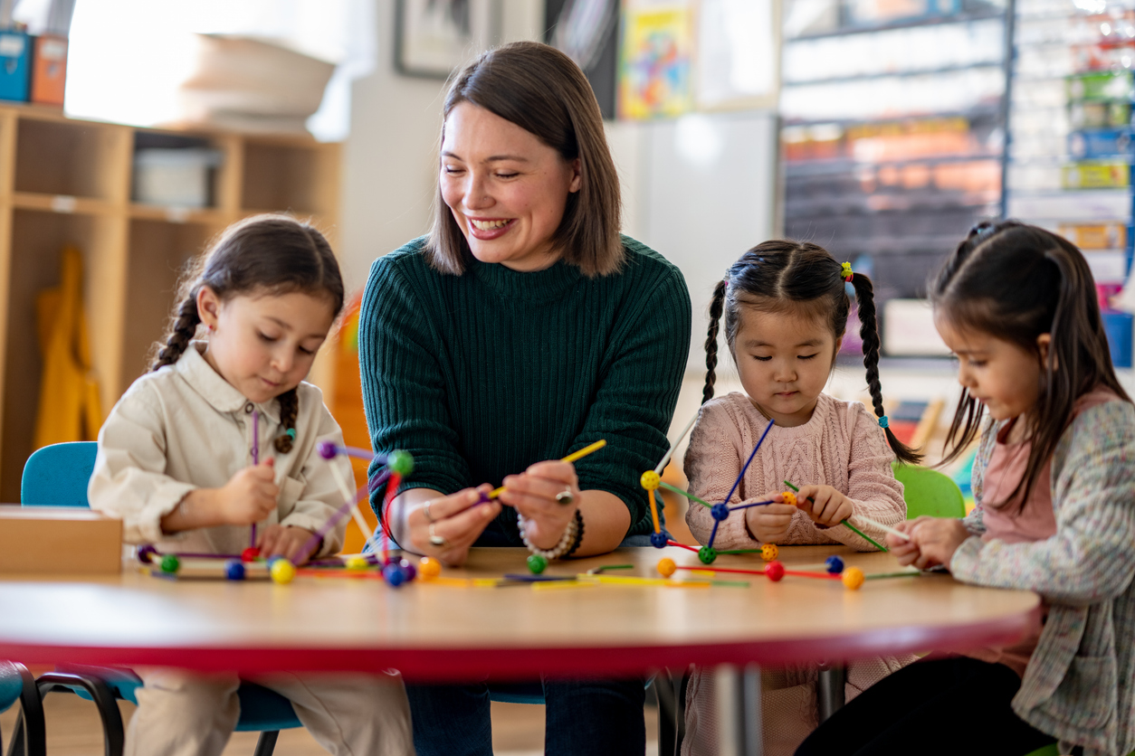 A Teacher Sitting at a Table With Three Kindergarten Students.