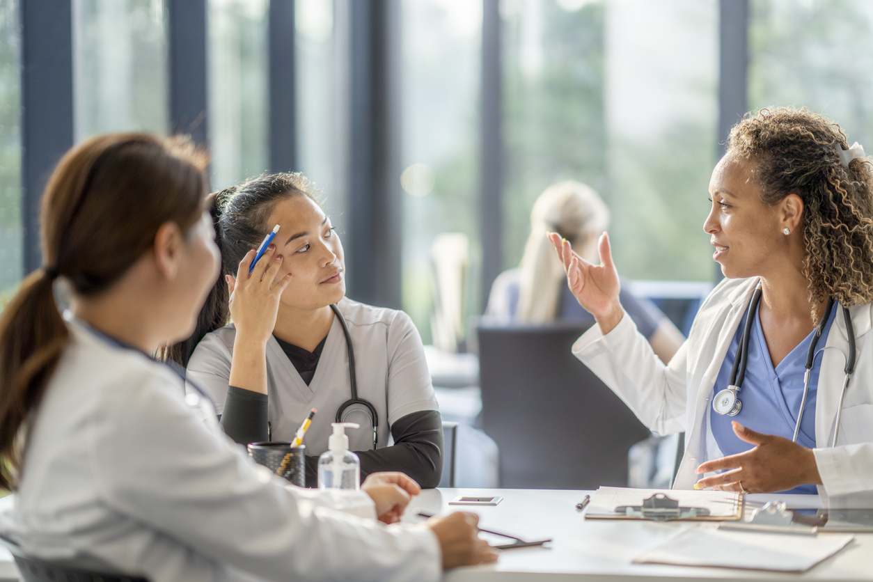 A Chief Nursing Officer Talks With Other Nurses Sitting at a Table.