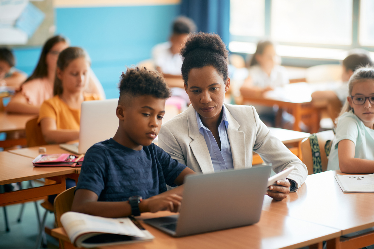 A Teacher Helps a Student Use a Laptop Computer During Class.