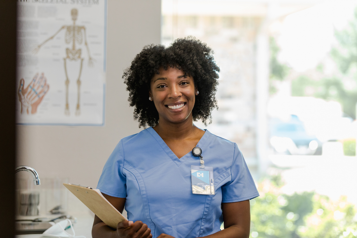 A Smiling Nurse Practitioner Holds a Clipboard in a Hospital Room