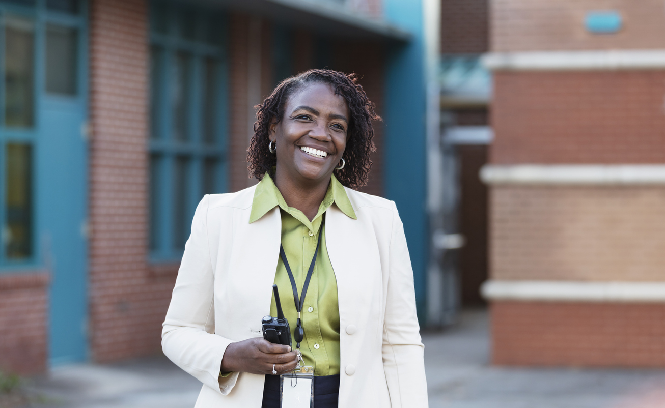 A smiling school principal stands outside of a school building.