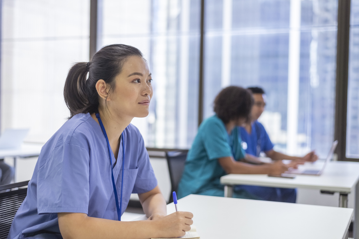 A Nursing Student Takes Notes During a Lecture in a Classroom With Other Nursing Students.