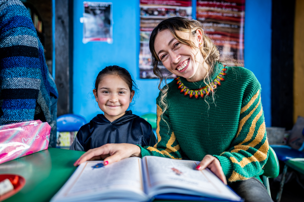 A smiling daycare teacher reads a book with a child.