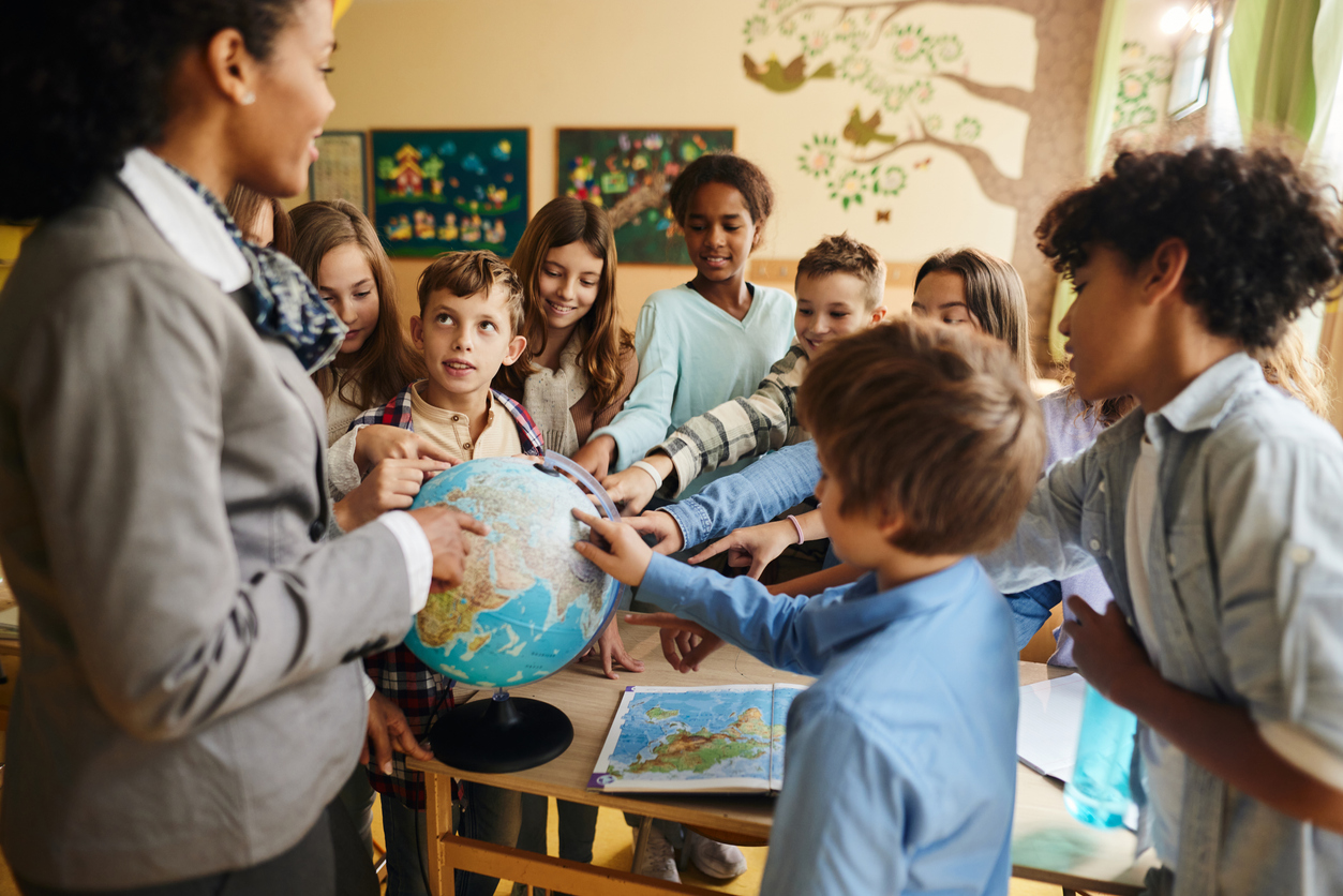 Students Stand Around a Teacher Holding a Globe in a Classroom.