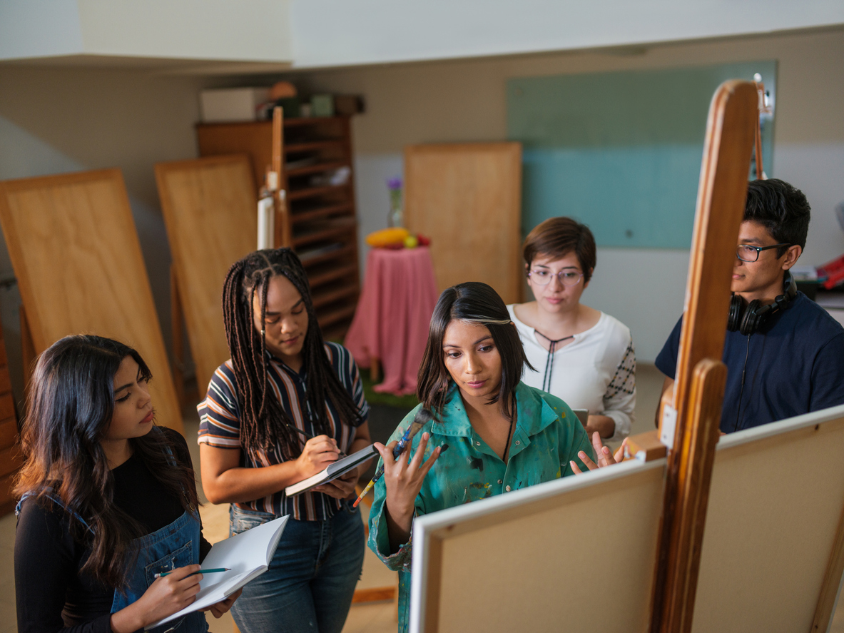 A high school art teacher demonstrates a technique to four students