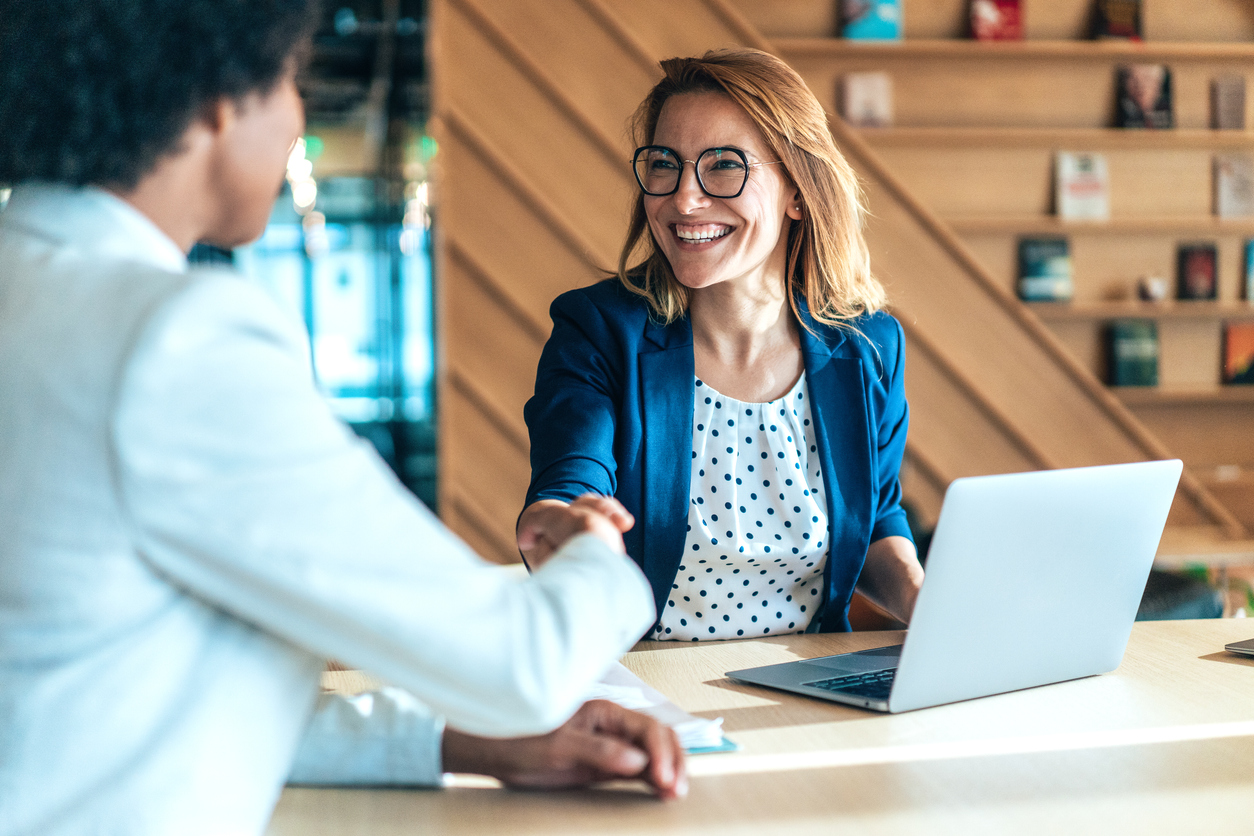 A hiring manager shakes hands with a candidate during a job interview.