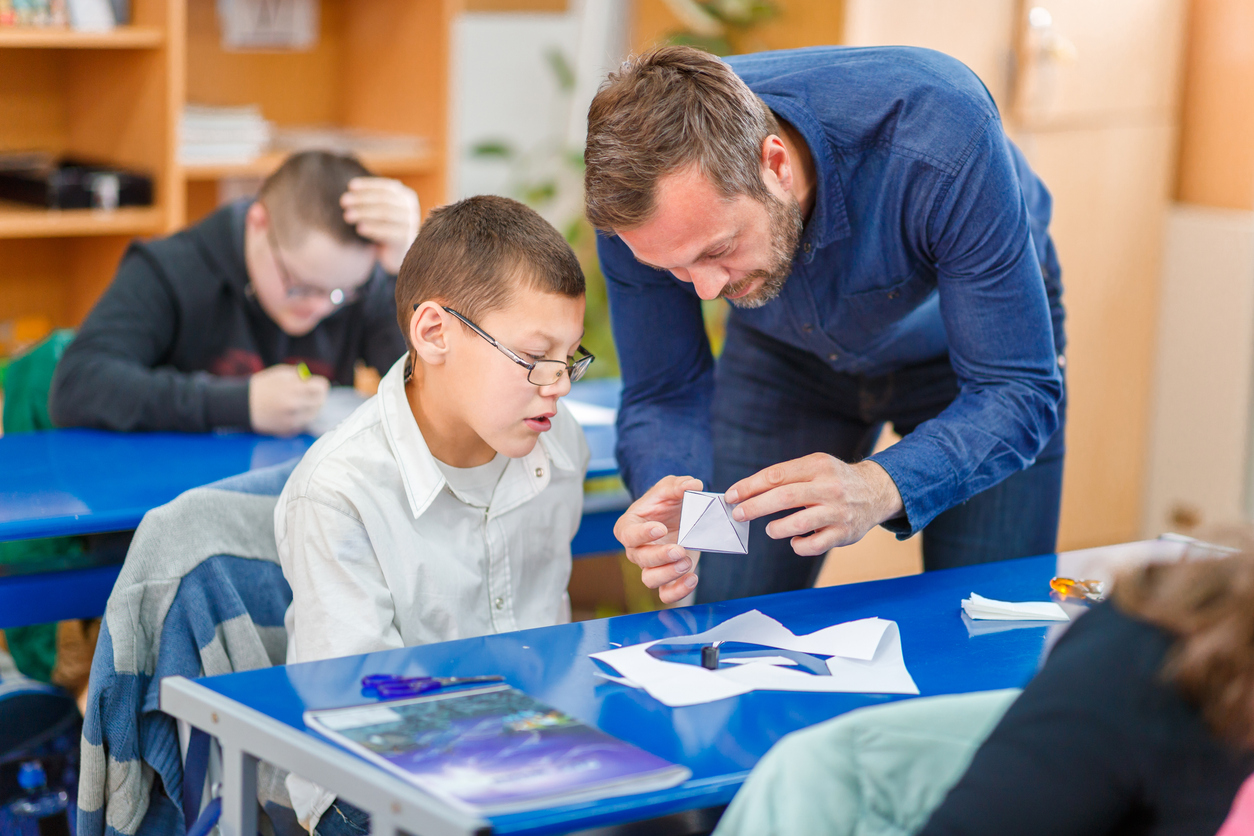 A teacher helps a student working on a craft project.
