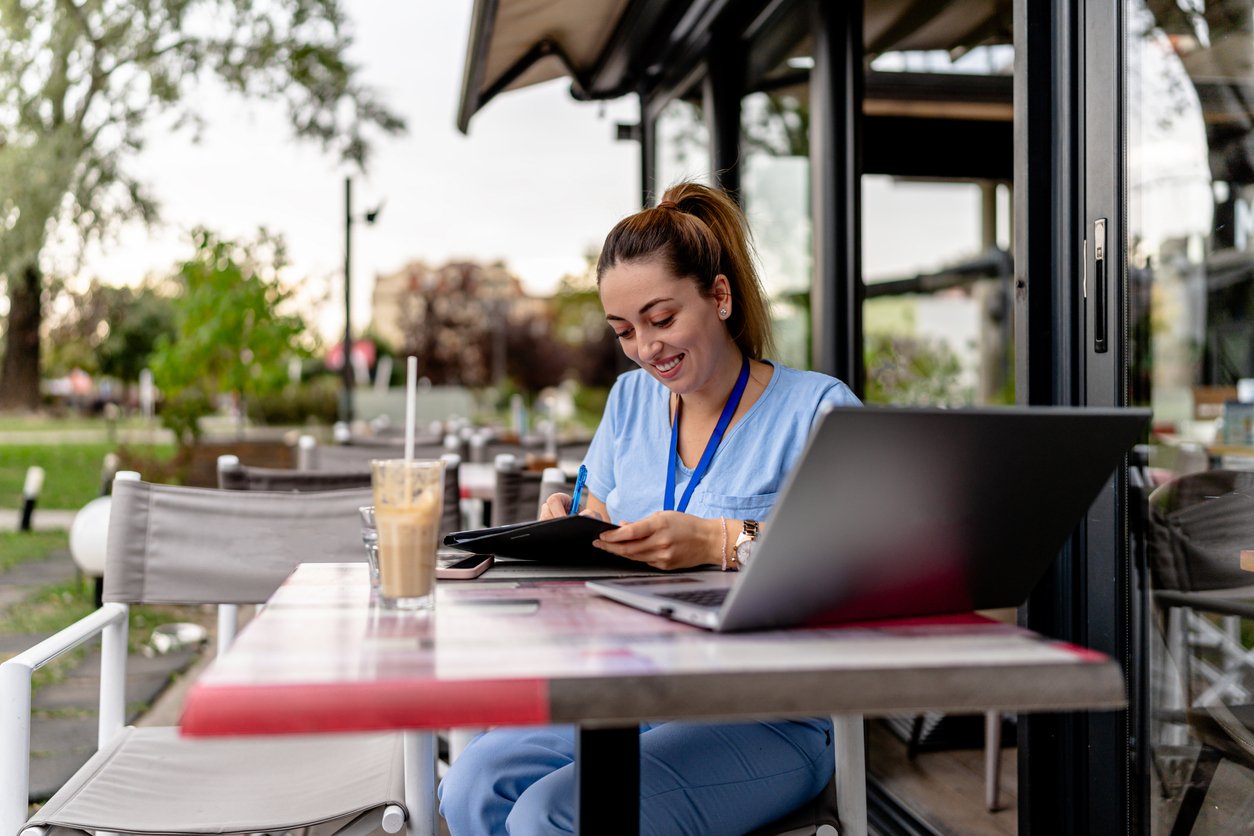An Online Msn Student Works at a Computer While Sitting Outside at a Cafe