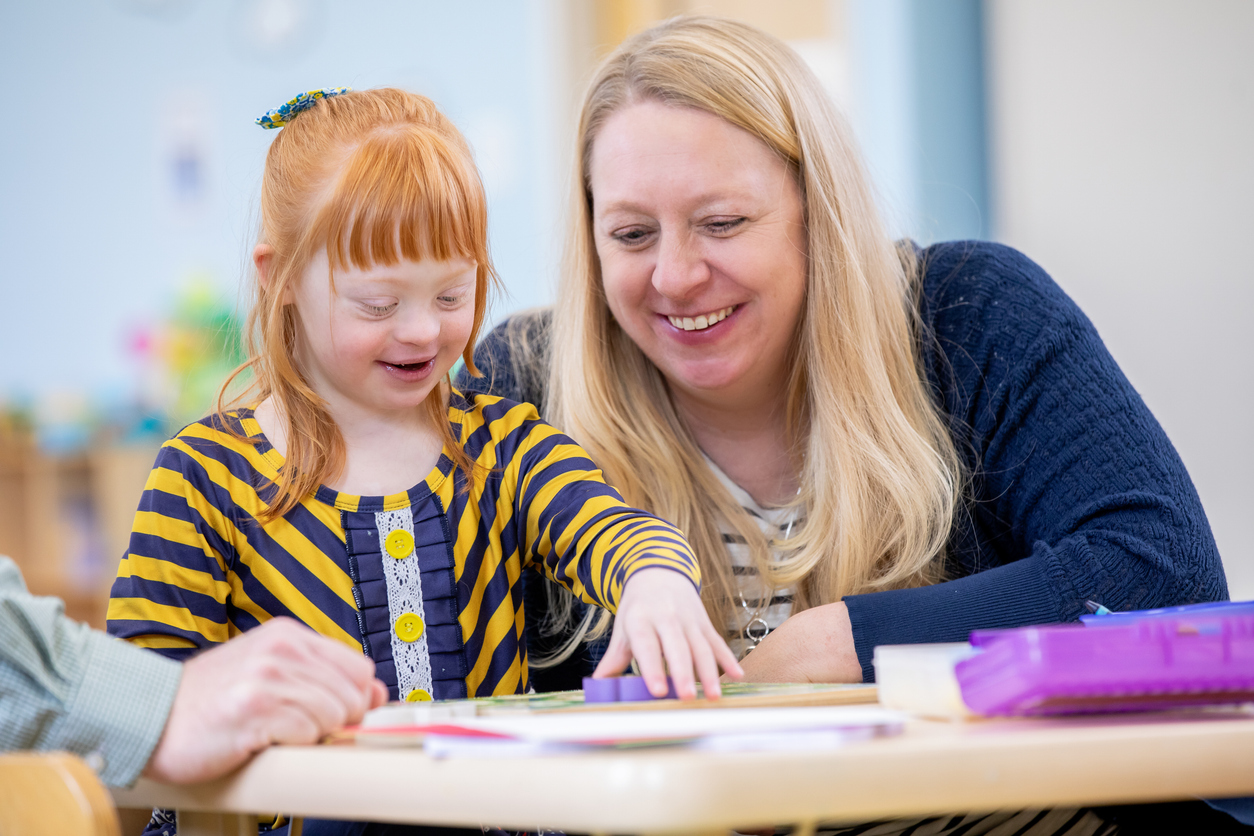 A Special Education Teacher Works With a Student at a Desk.