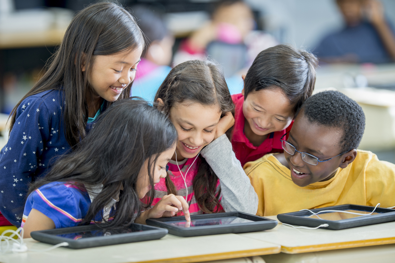 Five students play a game on a tablet in a classroom