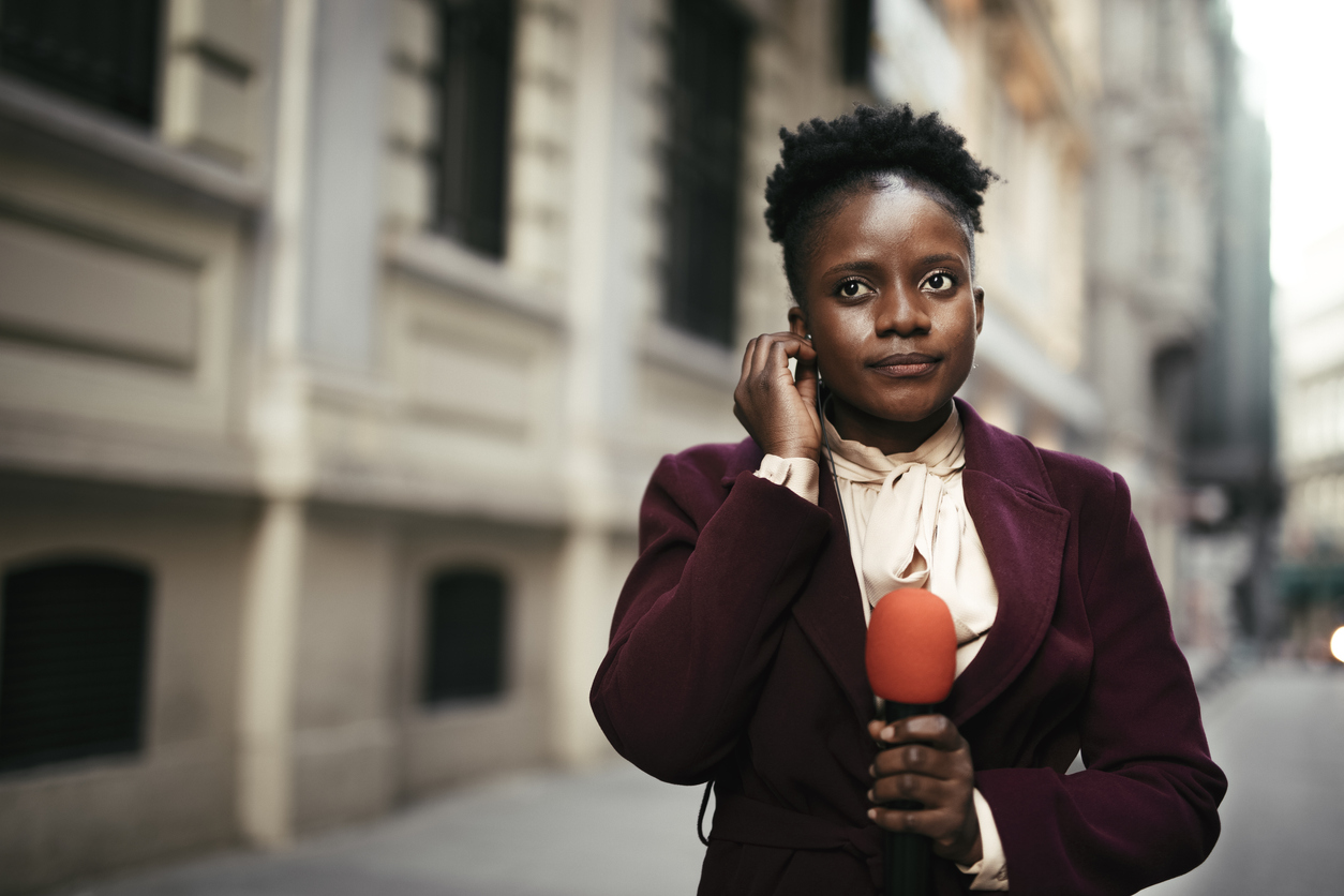 A reporter holds a microphone on the street.
