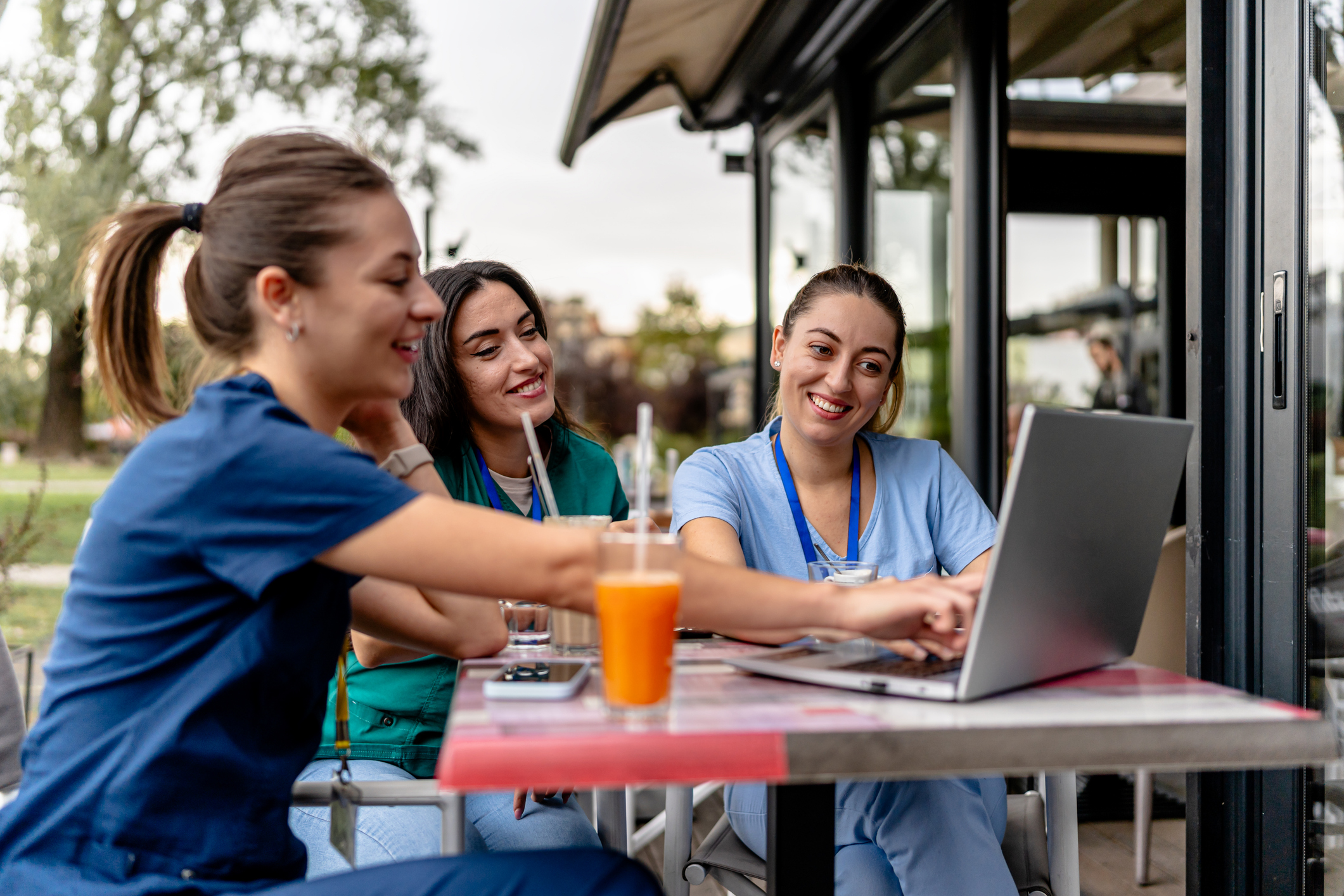 Three nursing students look at a laptop while sitting at a table outside.