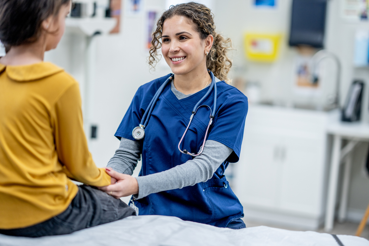 A Smiling Registered Nurse Holds Hands With a Young Patient.