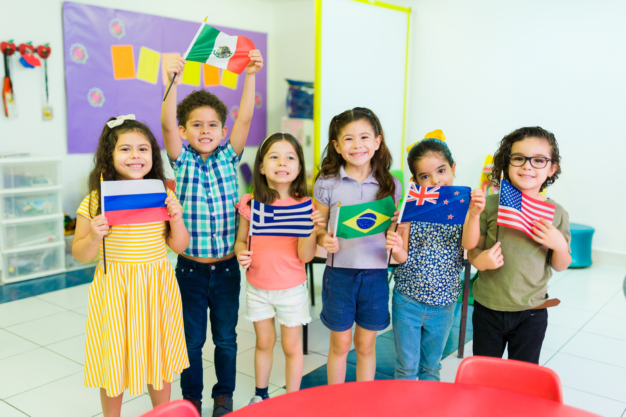 Six preschool students in a classroom holding flags from different countries.