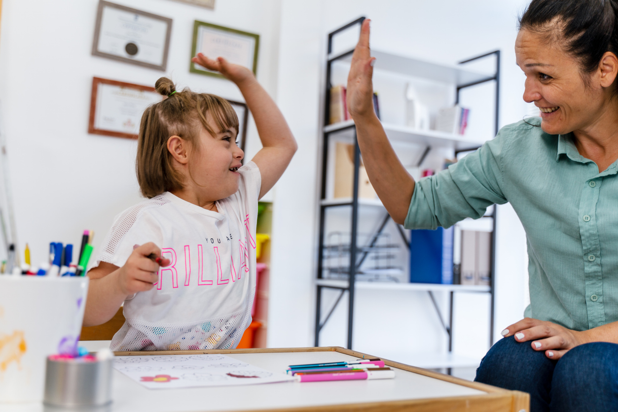 A special education teacher high-fives a student sitting at a desk.