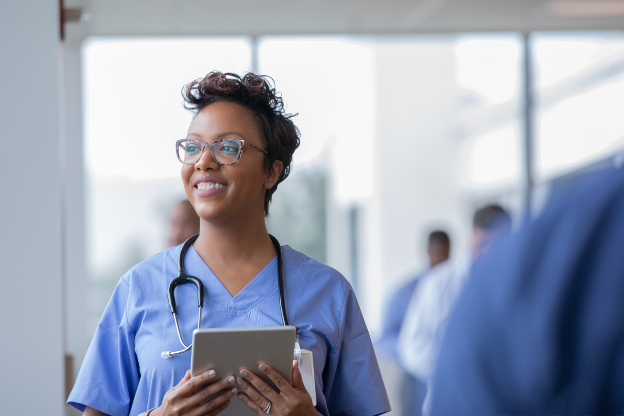 A smiling nurse holds a tablet in a hospital.