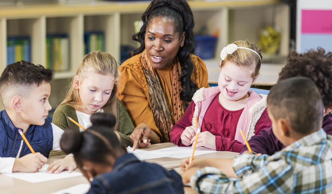 A Special Education Teacher Guides a Group of Students Who Are Sitting Around a Table and Writing..jpg