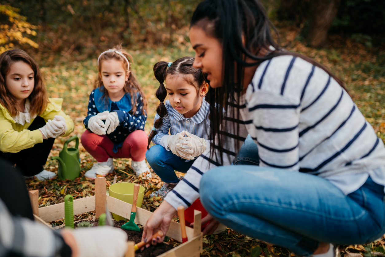 A teacher shows students how to tend to a garden during an after-school program.