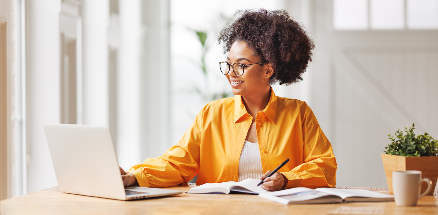 An Educational Researcher Writes in a Notebook While Consulting Survey Data on a Laptop..jpg