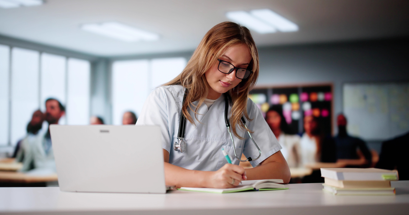 A Student Nurse Takes Notes While Watching a Lecture on a Laptop.