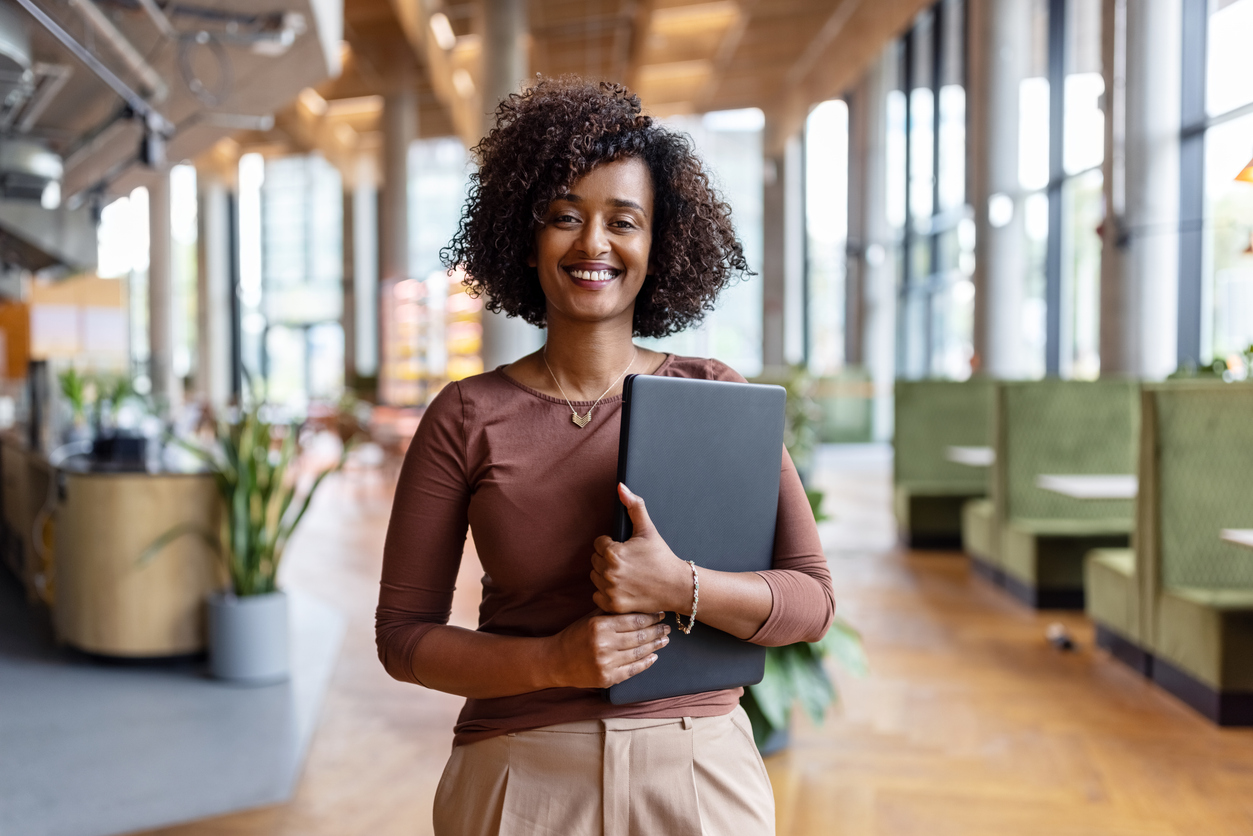 A smiling business person holds a tablet in an office.