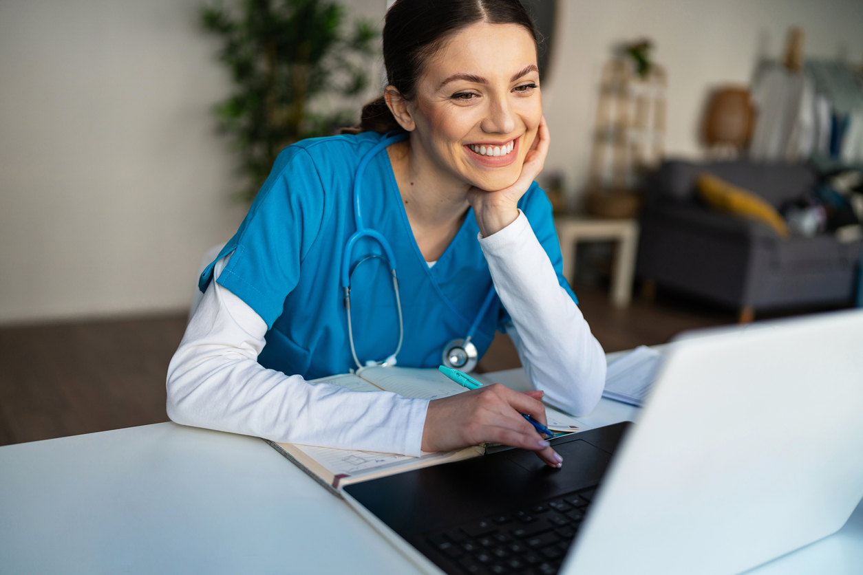 A smiling nursing student studies on a laptop.