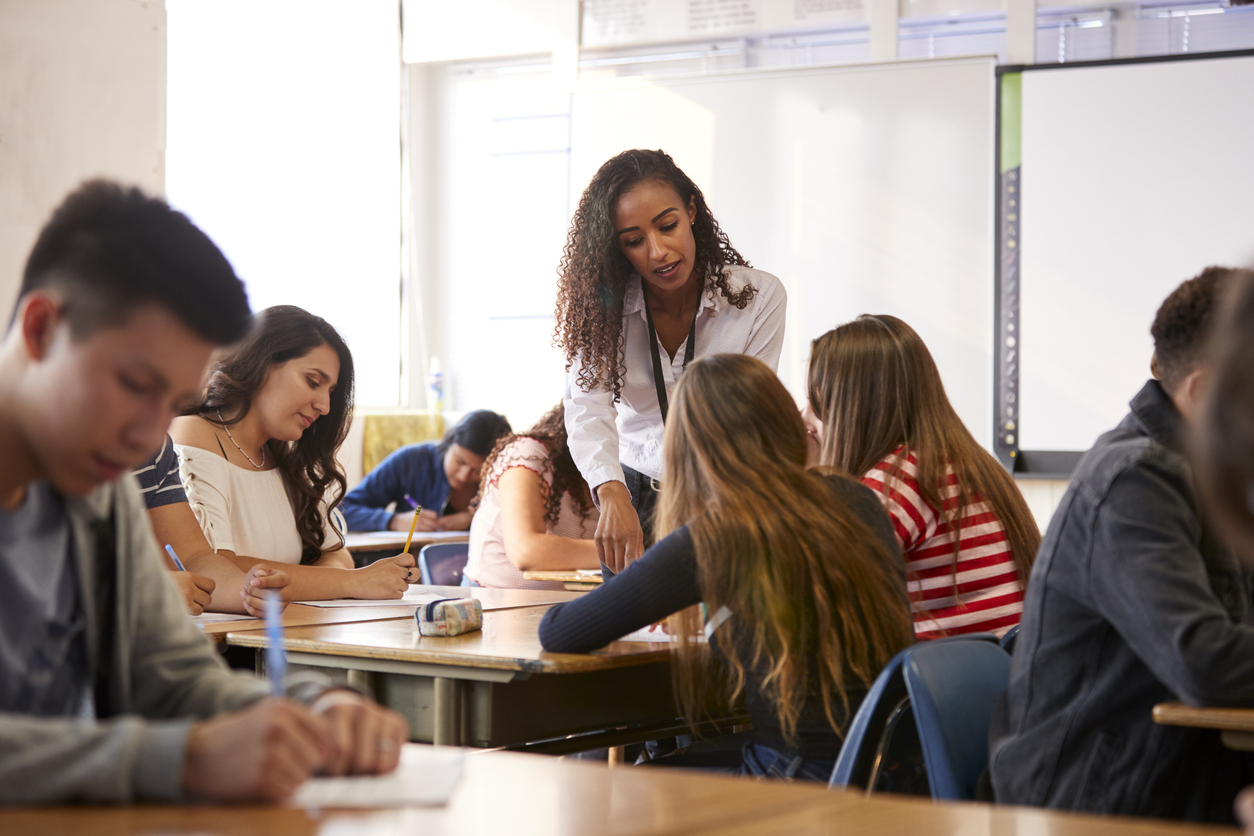A High School Teacher Points to a Student’s Paper in a Classroom.