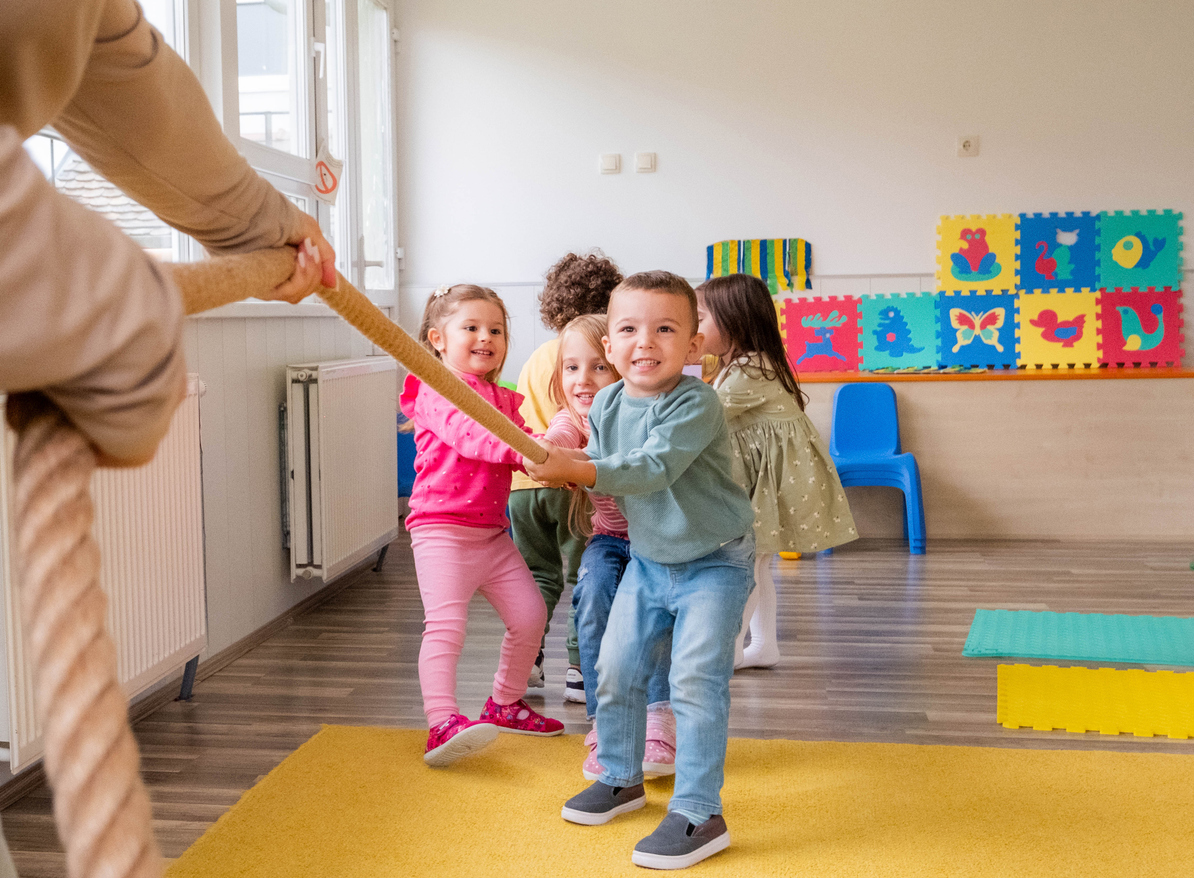A group of children and their teacher playing tug of war.