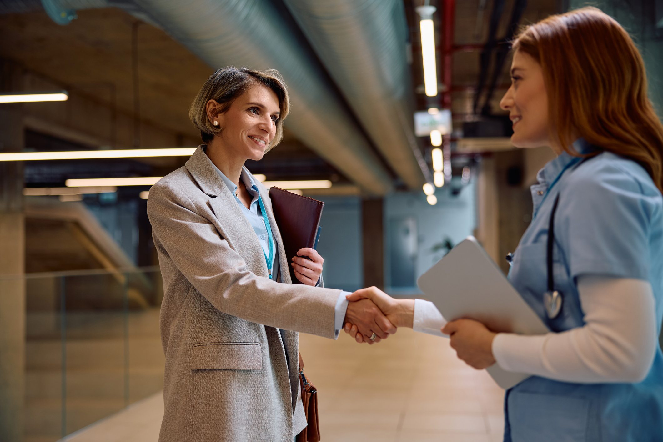 A hospital administrator shakes hands with a nurse in a hospital corridor.